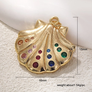 Detail of 15x16mm gold seashell charm with colorful gems on a white stone background