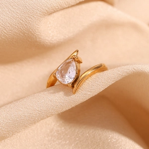 Macro detail of 18K gold plated wing ring with pear cut cubic zirconia on beige fabric