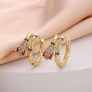 Detailed macro view of gold snake hoop earrings with zircon pavé and red gemstones
