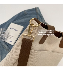 Detailed view of polished gold alloy hooks and brown strap on an off-white canvas tote