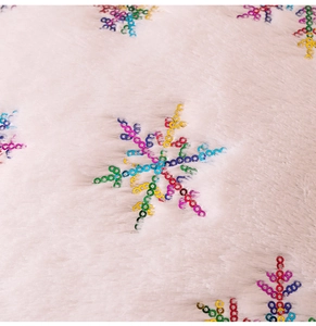 Macro shot of plush beige fabric with colorful snowflake sequins and soft textures