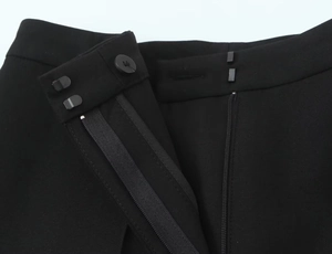 Close-up of black trousers featuring a resin button, metal hook, and zipper closure