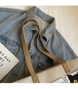 Detailed close-up of a beige canvas tote bag with slim khaki leather straps on denim