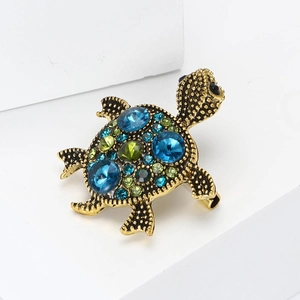 Vintage turtle brooch in bronze finish with blue and green rhinestones on white stand