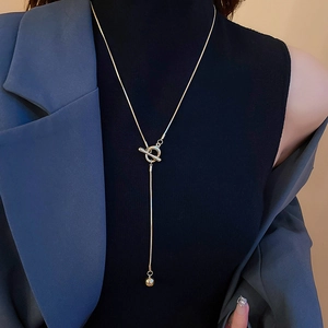 Macro shot of gold OT buckle necklace with metal bead pendant on model's dark clothing
