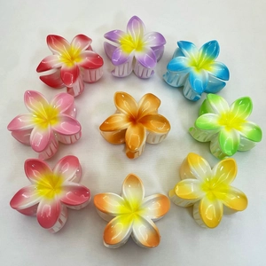 Top view of nine colorful plumeria flower hair claws arranged in a circle on white background