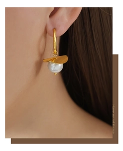 Detail of gold-plated hoop earring with wavy disc and lustrous pearl on a model