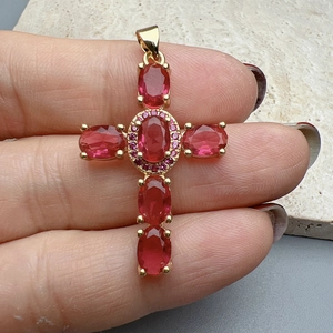 Close-up of gold cross pendant with red gemstones and pink crystal accents held by hand