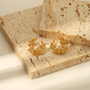 Elegant gold wheat leaf earrings in stainless steel on high-end stone display pedestal