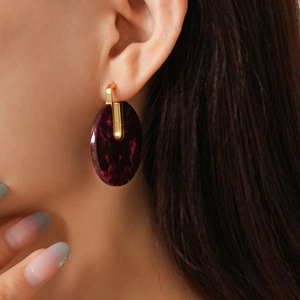 Close-up of circular burgundy marble acetate earrings with 18K gold-plated C-shaped studs