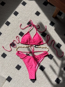 Rose pink triangle bikini set with white shell chain detail laid on textured rug