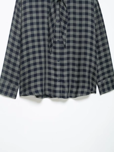 Dettaglio di camicia a quadri con colletto con fiocco e chiusura frontale a bottoni