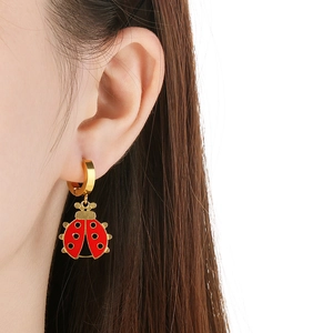 Close-up of cute red enamel ladybug charm earring worn on a golden stainless steel hoop