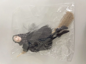Detail view of a Halloween witch doll hanging decoration on a wooden broom in packaging
