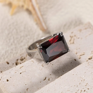 Close-up of a silver ring with red rectangular gemstone on a porous natural stone