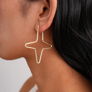 Close-up of model wearing gold cross star stud earrings with a minimalist geometric design