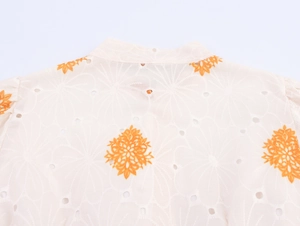 Dettaglio del tessuto traforato con ricamo floreale arancione su un abito camicia
