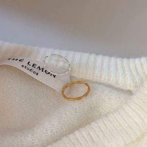 Close-up of minimalist woven silver and gold open rings on a white knitted sweater