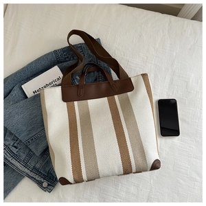 Close-up of the large canvas tote bag with vertical stripes and leather corner accents