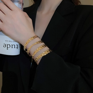 Detail of wide gold plated cuff bracelet with wave texture on model's wrist with black suit