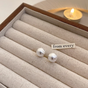 Macro shot of minimalist round white pearl stud earrings inside a wooden jewelry box