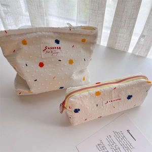 Detail of canvas makeup bag set with colorful embroidered dots on textured fabric