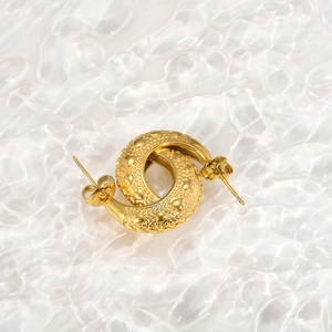 Close-up of gold stud earrings with heart texture on a water ripple surface