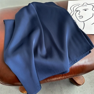 Detail of navy blue satin silk scarf with glossy texture on a leather surface