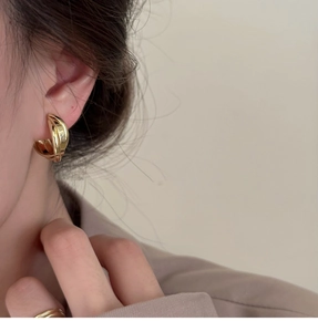 Gros plan de boucles d'oreilles clips dorées croisées au fini métallique sur modèle