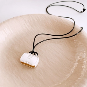 Detailed close-up of a white handbag-shaped pendant with gold edges on a ceramic tray