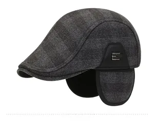 Detailed side view of grey plaid winter cap with ear flaps and metal letter E detail