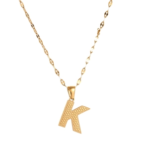 Detail shot of a golden letter K pendant with a textured surface on a delicate chain