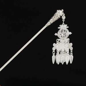 Detailed view of silver Hmong style hair pin with hollow filigree and tassel elements