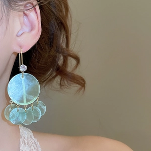 Detail of light green mother-of-pearl tassel earrings with zircon studs on female model
