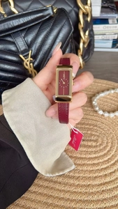 Detail view of a luxury women's gold square watch with a burgundy leather strap and dial