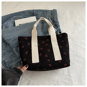 Detail of black corduroy tote bag with strawberry print and cream canvas handles