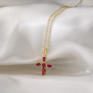 Détail d'un collier croix doré orné de cinq zircons rouges en forme de poire sur soie
