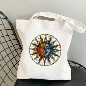 White canvas tote bag with artistic mosaic sun and moon print on a black metal chair