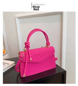 Detail of rose red woven shoulder bag featuring a knotted handle and golden swivel lock