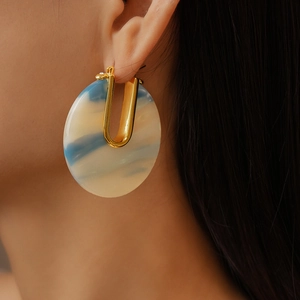 Close-up of woman wearing U-shaped 18k gold plated earrings with blue-white acetate rings