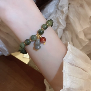 Close-up of green jade bead bracelet with gourd charm worn on a female wrist