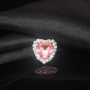 Macro shot of pink heart crystal ring with diamond halo on black satin background