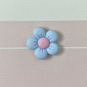 Macro detail of a light blue matte flower resin charm with a pink center on a striped surface