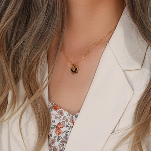 Detail of a golden necklace featuring a black butterfly pendant worn by a model