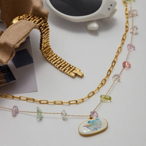 Detail of layered gold necklace with colorful natural stones and a white betta fish pendant