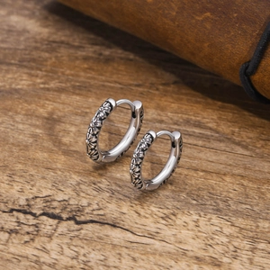 Macro detail of vintage silver hoop earrings with embossed daisy floral pattern carvings