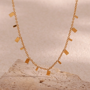 Close-up of a 18K gold plated necklace with small rectangular pendants on textured stone