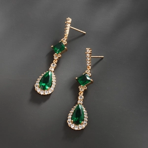 Macro detail of emerald-cut and pear-shaped green gemstones set in gold-plated drop earrings