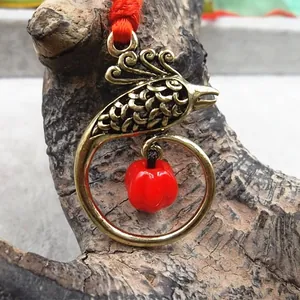 Macro shot of retro bird charm with red bead on brown tree bark background