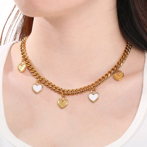 Gros plan d'un collier chaîne cubaine dorée avec breloques cœur blanc sur modèle